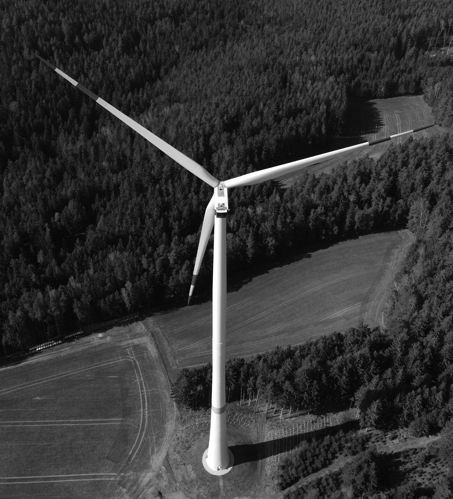 High-angle black and white aerial shot of a wind turbine amidst forest and fields in Pfreimd, Germany.